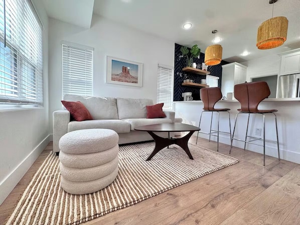 A living room with a sofa, ottoman, coffee table, and bar stools. - Coronado Historic Casita · King Bed · Private Yard · Phoenix (Phoenix)