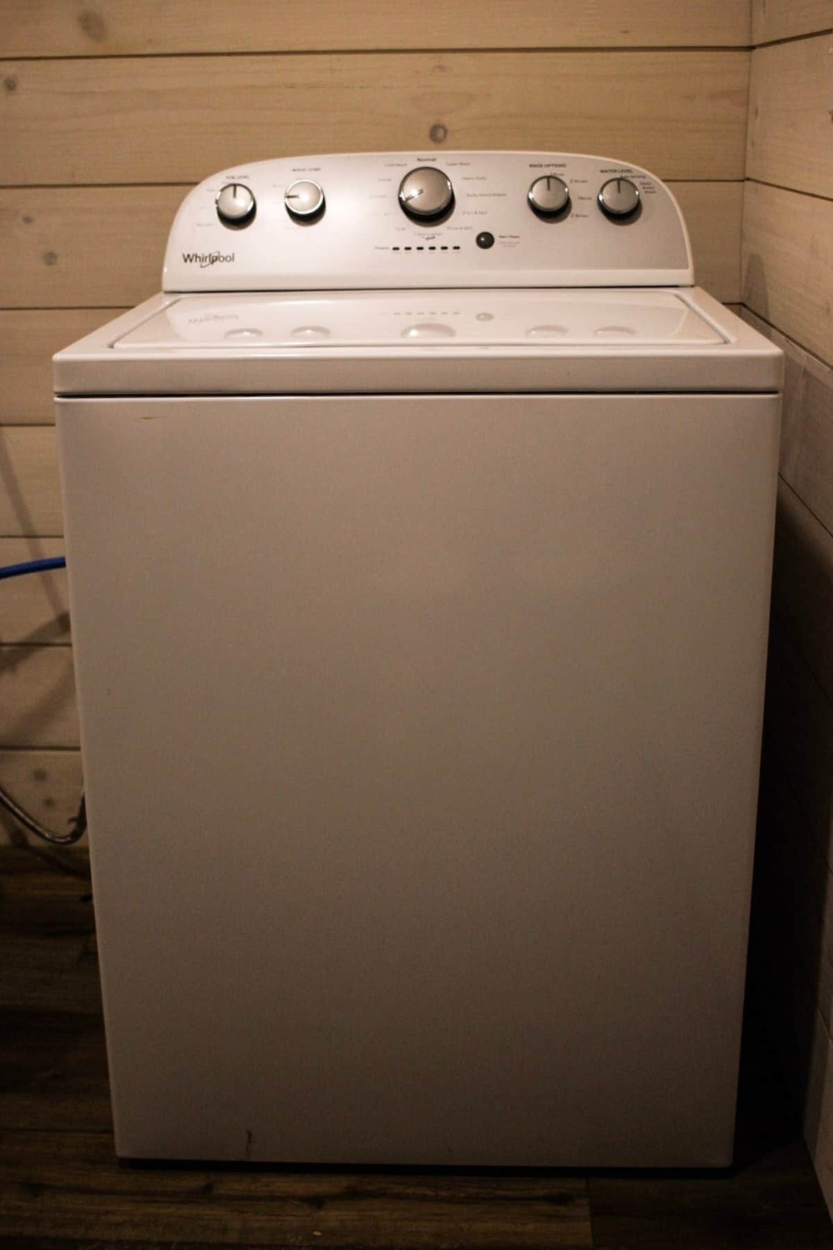 Una lavatrice Whirlpool in una stanza con pareti in legno e un cavo di alimentazione visibile.