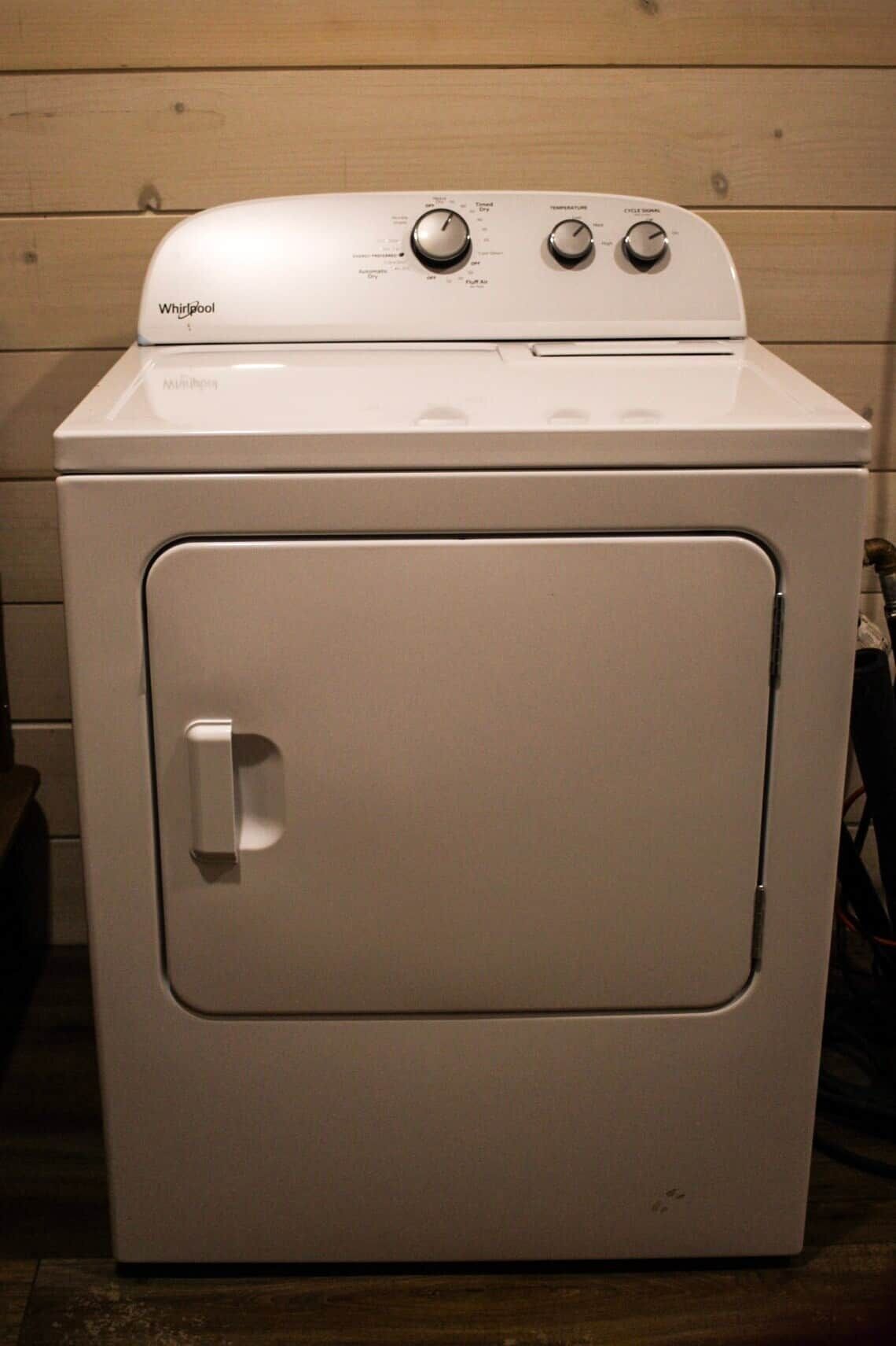 A Whirlpool washer with a front door, control panel with temperature and cycle settings, and a small handle on the door.