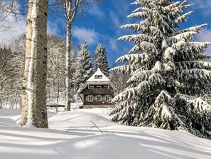 Eine verschneite Landschaft mit einer Holzhütte und schneebedeckten Bäumen.