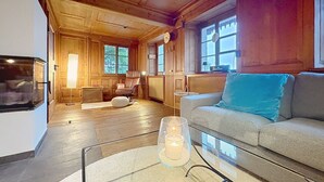 A cozy cabin interior with a wooden floor, a glass coffee table with candles, a leather chair, a sofa with a blue pillow, and a television mounted on the wall. - Wonderful private villa for 6 guests with WIFI and patio (Bärental)