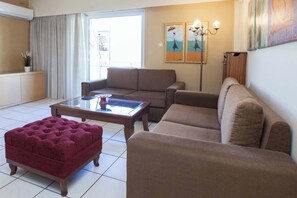 A living room with a sofa, ottoman, and a glass-top coffee table. - Elegant 2 Bd Apt with Balcony in Korydallos Square (Koridallos)