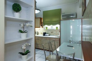 A kitchen with white cabinets, a dining table with chairs, a potted plant, and a window with a green blind. - Elegant 2 Bd Apt with Balcony in Korydallos Square (Koridallos)