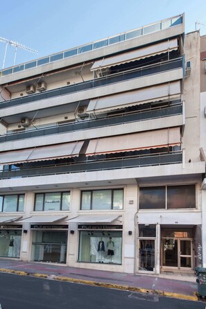 A multi-story building with storefronts on the ground level, including a visible store named 'Pull&Bear.' - Elegant 2 Bd Apt with Balcony in Korydallos Square (Koridallos)