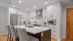 A modern kitchen with white cabinets, stainless steel appliances, and a central island with bar stools. - BergTraum Refined Alpine Escape in Spring Creek (Canmore)