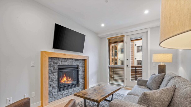 A living room with a fireplace, a flat-screen TV mounted above it, a sofa, and a coffee table. - BergTraum Refined Alpine Escape in Spring Creek (Canmore)