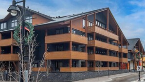 A multi-story hotel with balconies, a stone facade, and a pedestrian sign. - BergTraum Refined Alpine Escape in Spring Creek (Canmore)