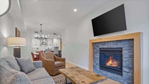 A modern living room with a fireplace, a sofa, a coffee table, and a television mounted on the wall. - BergTraum Refined Alpine Escape in Spring Creek (Canmore)