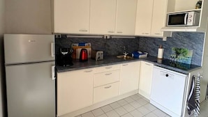 Una cocina moderna con armarios blancos, microondas integrado, refrigerador y lavavajillas.