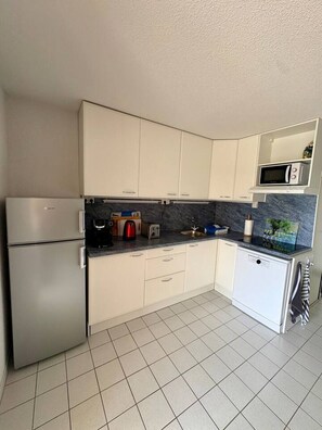 Eine moderne Küche mit weißen Schränken, einer eingebauten Mikrowelle, einem Kühlschrank und einem Geschirrspüler.