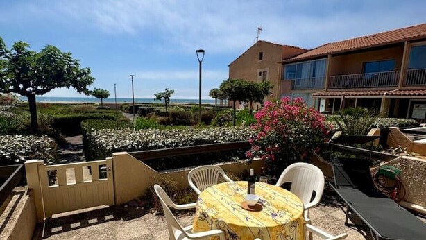 Un patio al aire libre con una mesa redonda y sillas, vista al mar y un edificio con balcón.