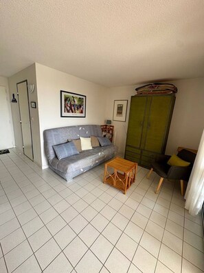 Ein Wohnzimmer mit einer Couch, einem kleinen Holztisch, einem grünen Schrank und einer Tür.