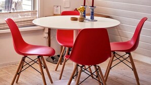 Una habitación con una mesa redonda, sillas rojas, una lámpara colgante y un cuadro en la pared.