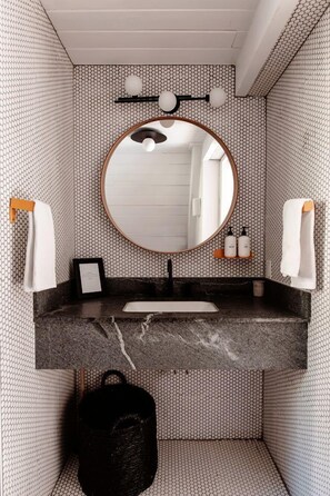 A bathroom with a round mirror, black countertop, and patterned walls.