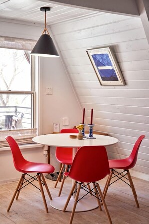 A room with a round table, red chairs, a pendant light, and a framed picture on the wall.