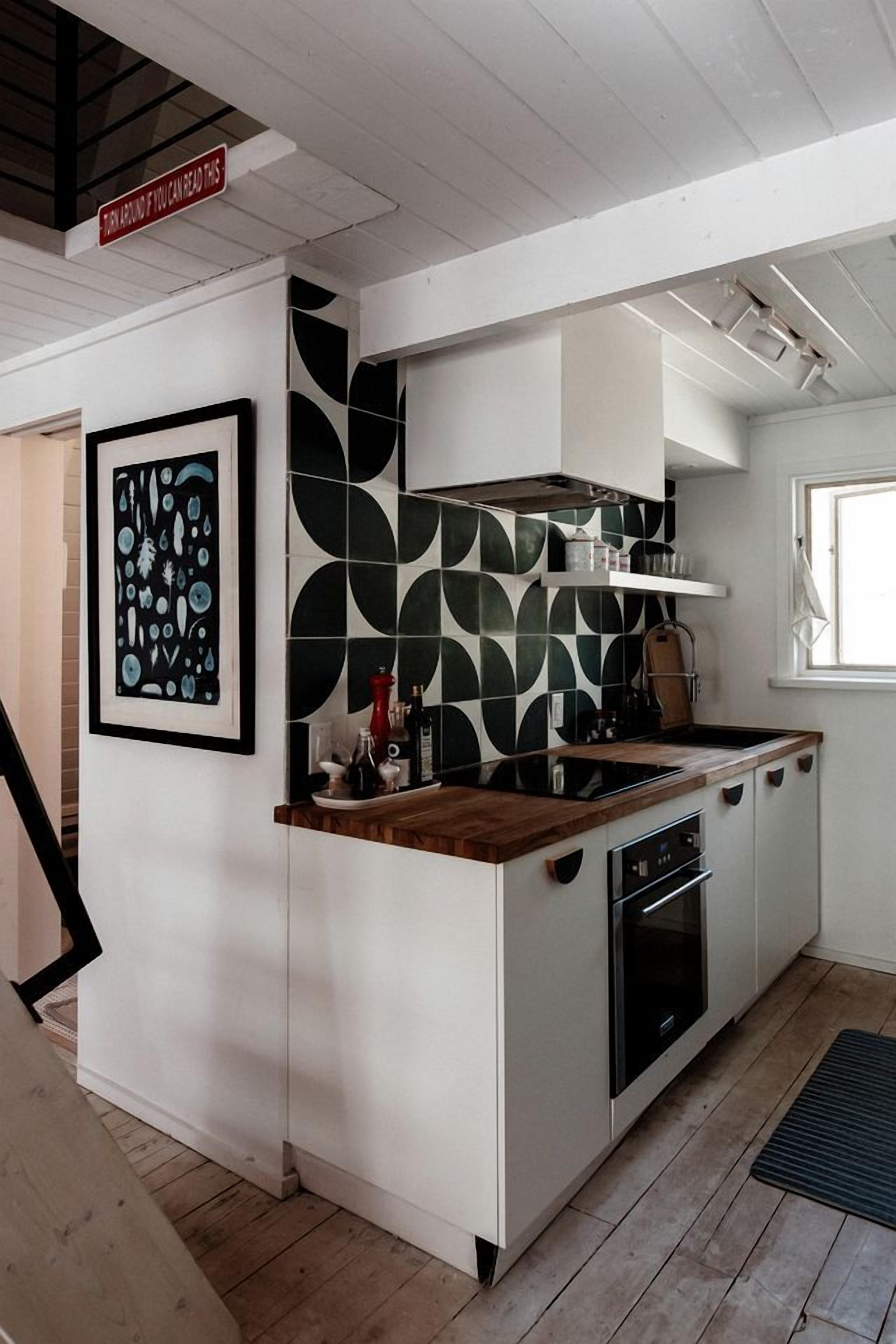 Cocina compacta con isla central, muebles blancos y salpicadero con estampado blanco y negro.