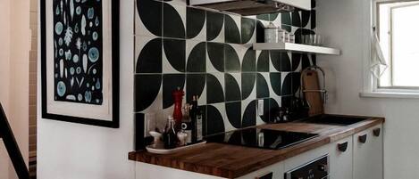 Cocina compacta con isla central, muebles blancos y salpicadero con estampado blanco y negro.