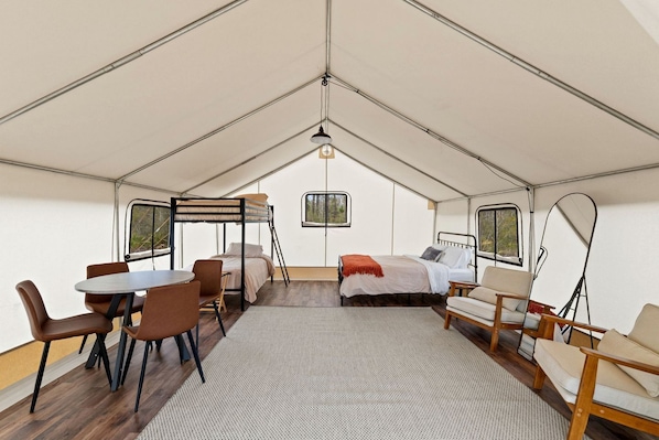 A tented accommodation with a bunk bed, a dining table, chairs, and a sofa.