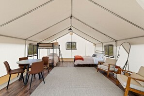 A tented accommodation with a bunk bed, a dining table, chairs, and a sofa.