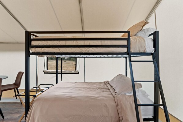 Una cama litera con escritorio y silla, una ventana, y vistas al exterior.