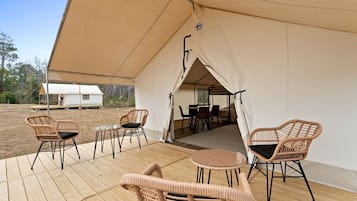 A covered outdoor seating area with wicker chairs and a table, connected to a tented structure.