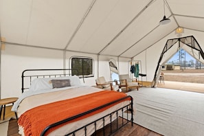 A tented accommodation with a bed, chairs, and a view of the outdoors.