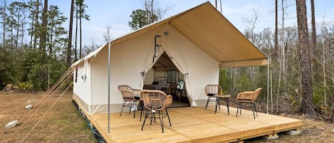 Un camping-car à plateforme avec un toit en forme de tente, une terrasse en bois et des chaises en osier.