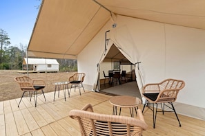 A covered outdoor seating area with wicker chairs and a table, connected to a tented structure.