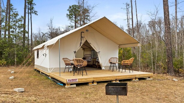 A tent with a flat roof, two wicker chairs, a small table, and a grill outside. - Outdoor Adventure Basecamp: World-Class Fishing, Hiking Trail & Pet-Friendly Fun in Wewahitchka, Florida (Wewahitchka)