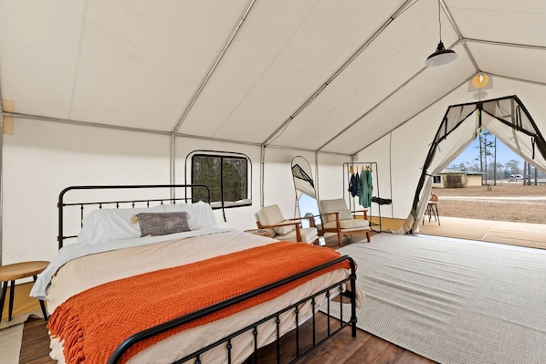Alojamiento con tienda de campaña, una cama, sillas y vistas al exterior.