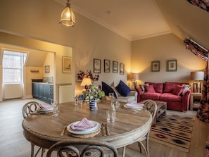 A dining area with a round wooden table set for four, a red sofa, and a kitchen in the background.