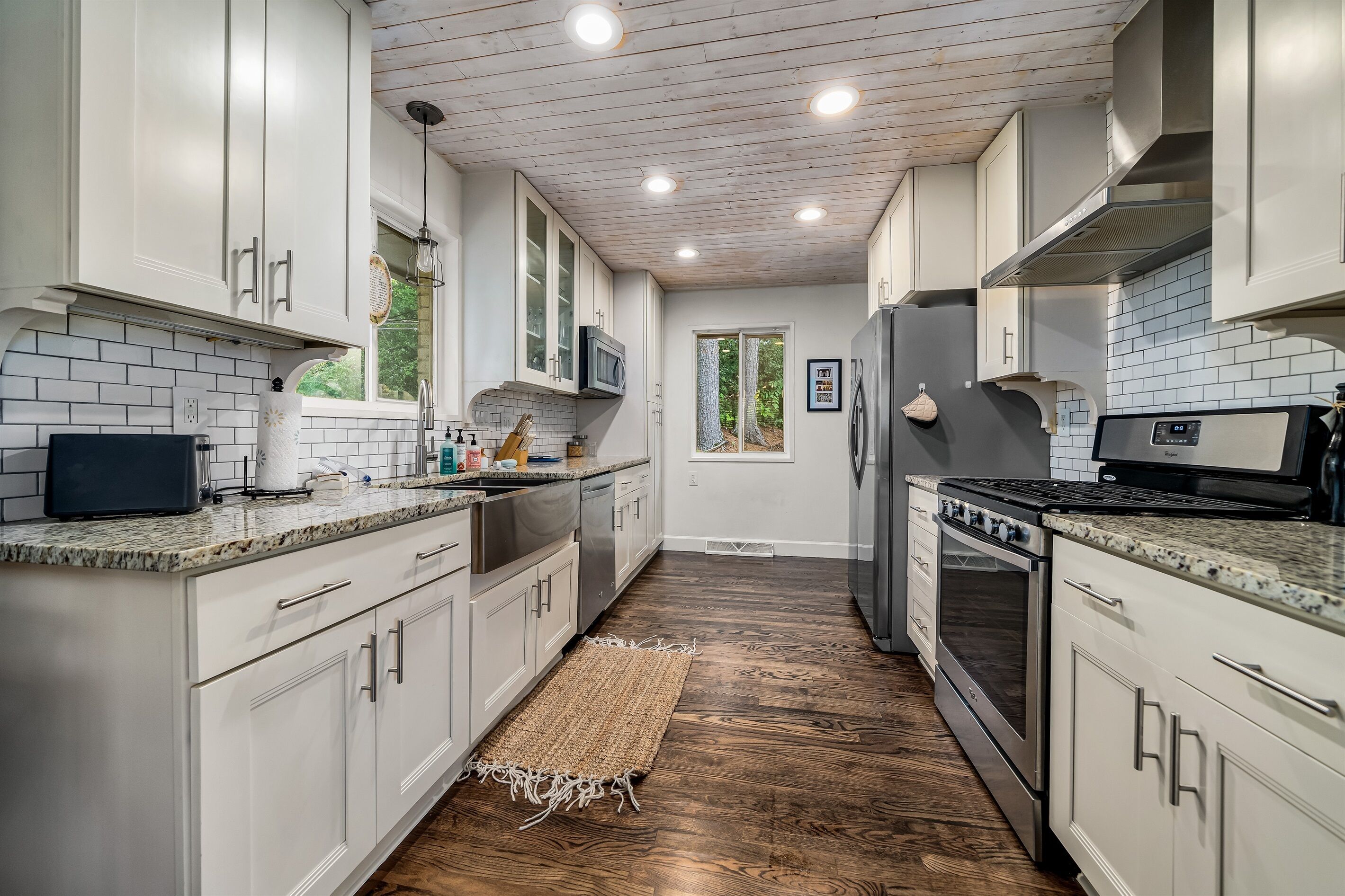 Une cuisine moderne avec des meubles blancs, un plancher en bois et une vue sur l’extérieur.