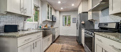 A modern kitchen with white cabinets, a wooden floor, and a view to the outside.