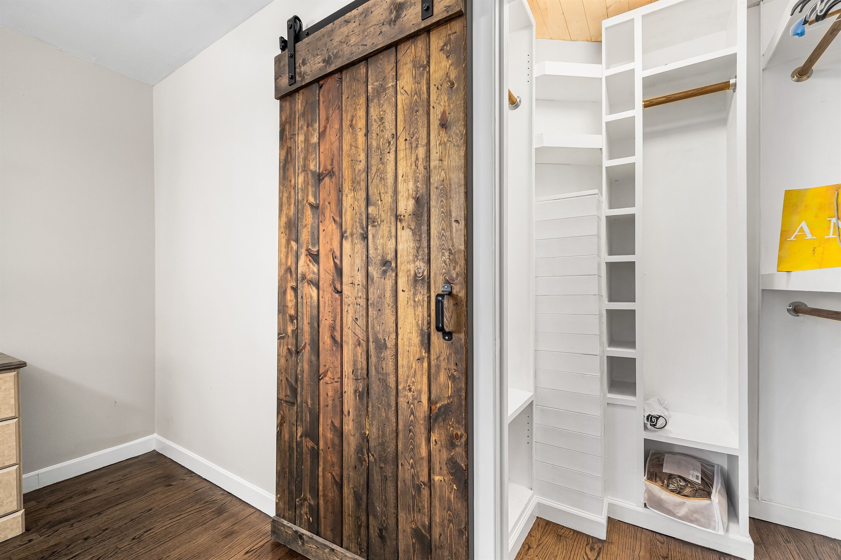 Una habitación con puerta corrediza de madera, paredes blancas y un armario blanco con estantes.