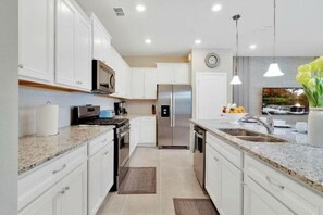A modern kitchen with white cabinets, stainless steel appliances, granite countertops, and pendant lighting. - 7495 OL - SOLTERRA RESORT (Davenport)