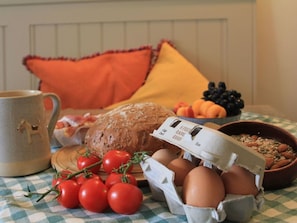 Ein Frühstückstisch mit Brot, Eiern, Tomaten, einer Obstschale und einer Tasse.