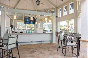 A covered outdoor seating area with a bar, chairs, and a TV screen. - 3073 PP - STOREY LAKE (Kissimmee)