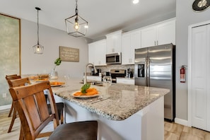 A modern kitchen with granite countertops, stainless steel appliances, and wooden chairs. - 3073 PP - STOREY LAKE (Kissimmee)
