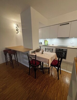 A compact kitchen with white cabinets, a dining table with chairs, and a wooden floor. - Cozy and Modern Apartment in a Great Location (Lausanne)