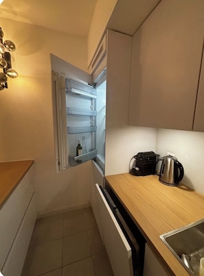 A compact kitchen with a built-in refrigerator, a kettle, and a sink. - Cozy and Modern Apartment in a Great Location (Lausanne)