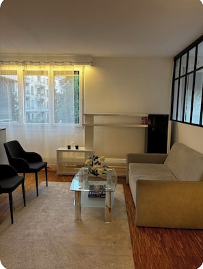 Ein Wohnzimmer mit einer Couch, zwei Sesseln, einem Glastisch und einem Fernsehschrank.