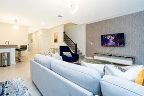 A modern living room with a sofa, a blue chair, a TV, and a staircase. - 1070 SS - CHAMPIONS GATE (Kissimmee)
