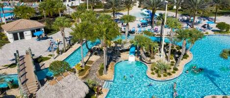 A resort with a large central pool, palm trees, and a thatched-roof structure.