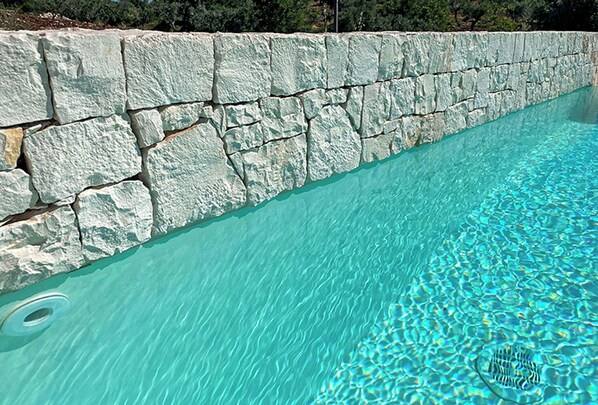 A stone pool with clear water, surrounded by a stone wall. - Trullo with infinity pool amid olive groves (Alberobello)