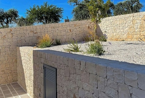 A stone wall with a door, surrounded by gravel and plants. - Trullo with infinity pool amid olive groves (Alberobello)