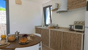 A modern kitchen with a dining table set for breakfast, a built-in oven, and a window overlooking the garden. - Trullo with infinity pool amid olive groves (Alberobello)