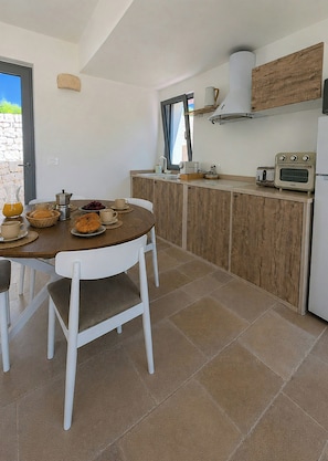 Eine moderne Küche mit Esstisch, gedeckt für ein Frühstück, einem eingebauten Backofen und einem Fenster mit Blick auf den Garten.