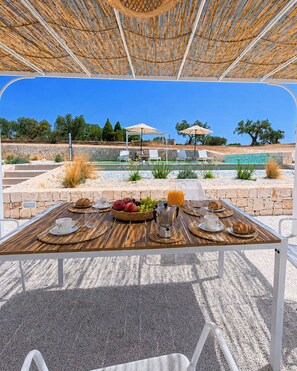 Een terras met een ontbijttafel, met uitzicht op een zwembad en ligbedden.