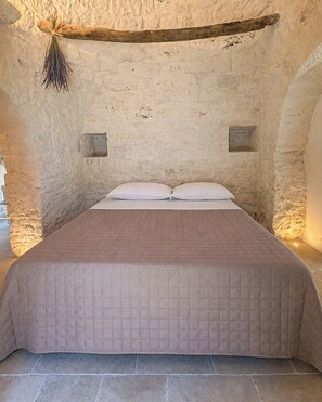 A bed with a quilted bedspread in a room with stone walls and a wooden beam ceiling. - Trullo with infinity pool amid olive groves (Alberobello)