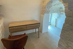 A room with a wooden desk, a cushioned chair, and a stone wall. - Trullo with infinity pool amid olive groves (Alberobello)